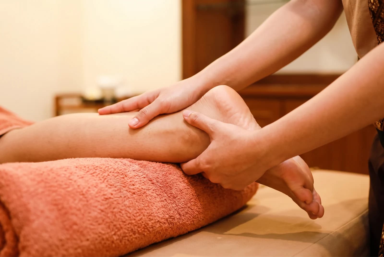 Hands supporting a guest’s calf and ankle on a coral towel