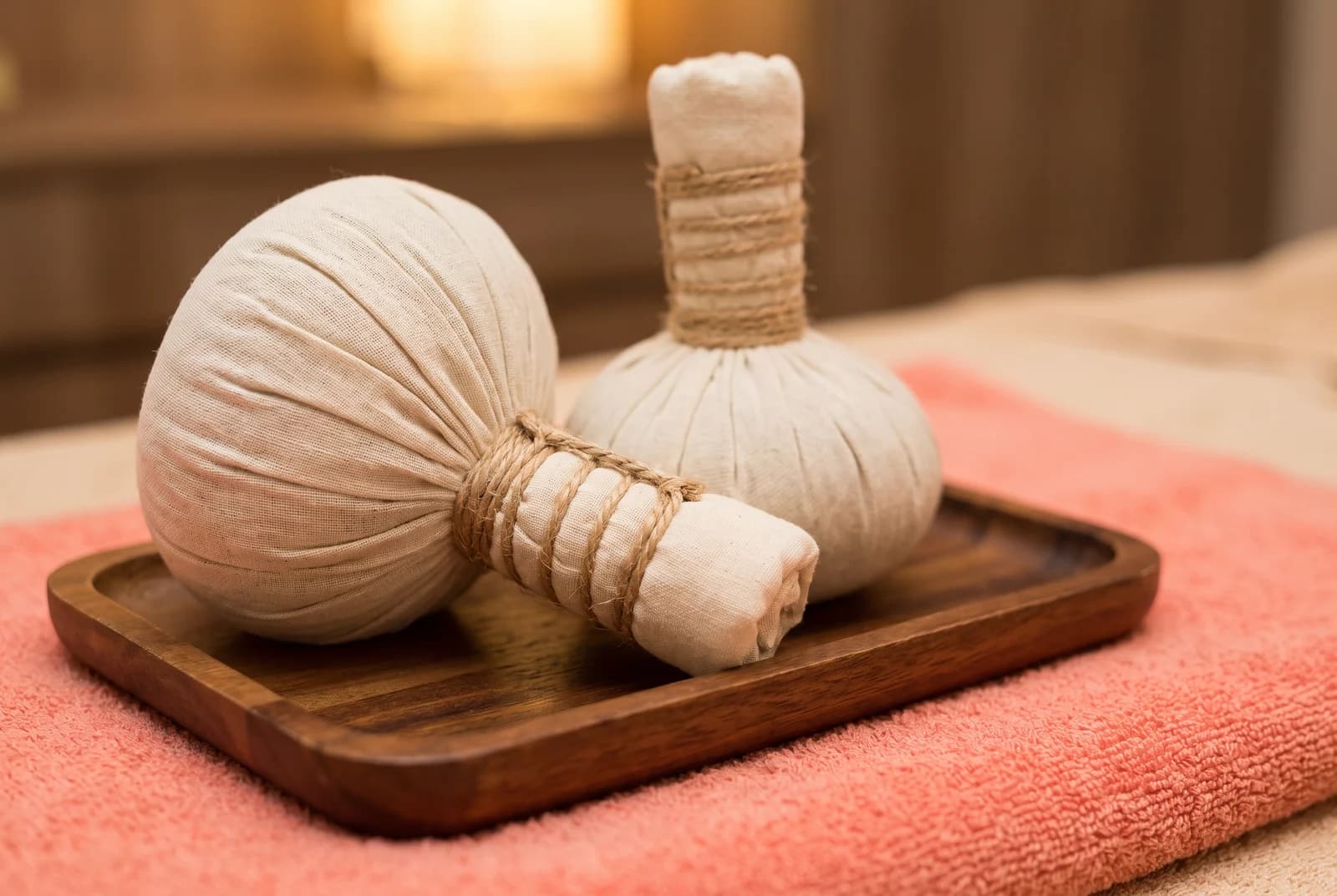 Two cotton herbal compress bundles on a wooden tray